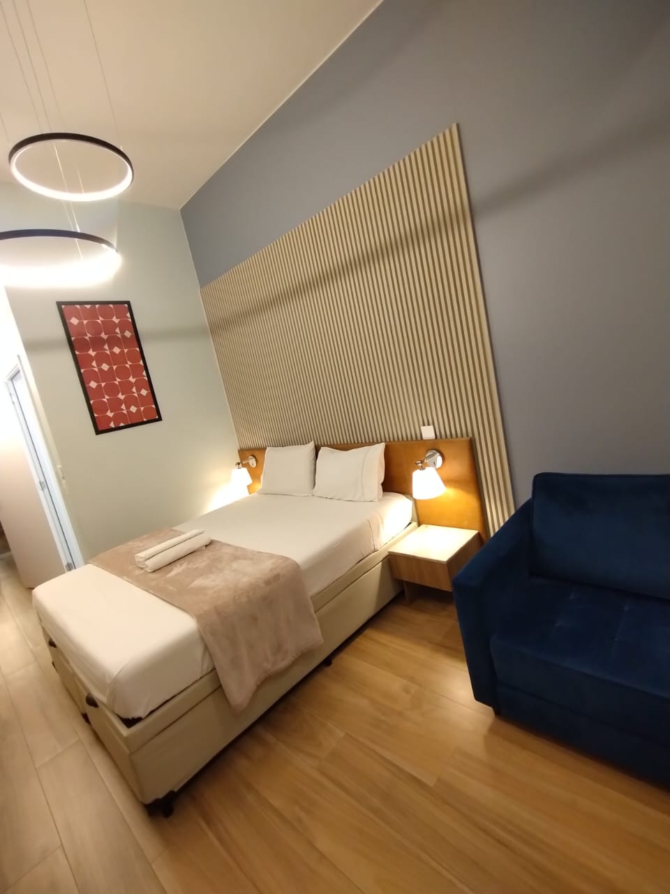 Quarto de hotel moderno com cama de casal, cabeceira ripada e poltrona azul